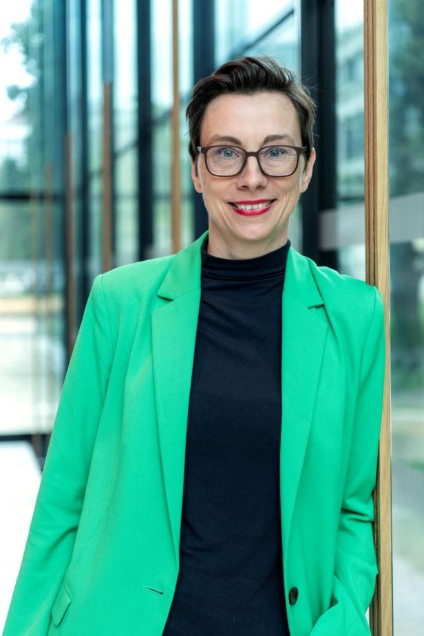 Eine Frau mit Brille und grünem Blazer lächelt in die Kamera.