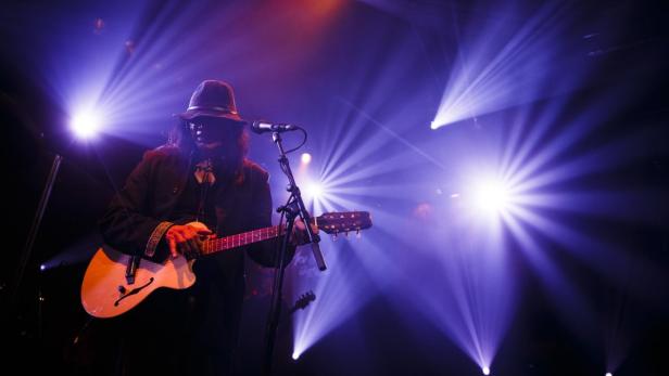 Ein Gitarrist mit Hut spielt auf einer Bühne im Scheinwerferlicht.