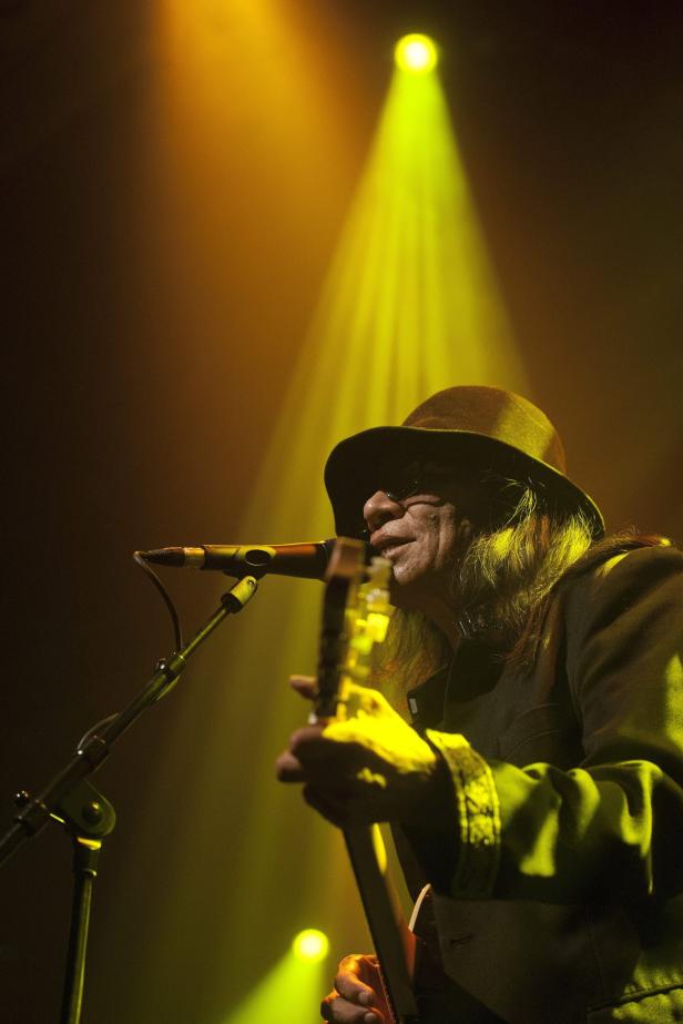 Ein Musiker mit Hut spielt Gitarre im gelben Scheinwerferlicht.