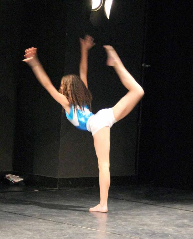 Eine junge Tänzerin führt eine Ballettpose auf einer Bühne auf..