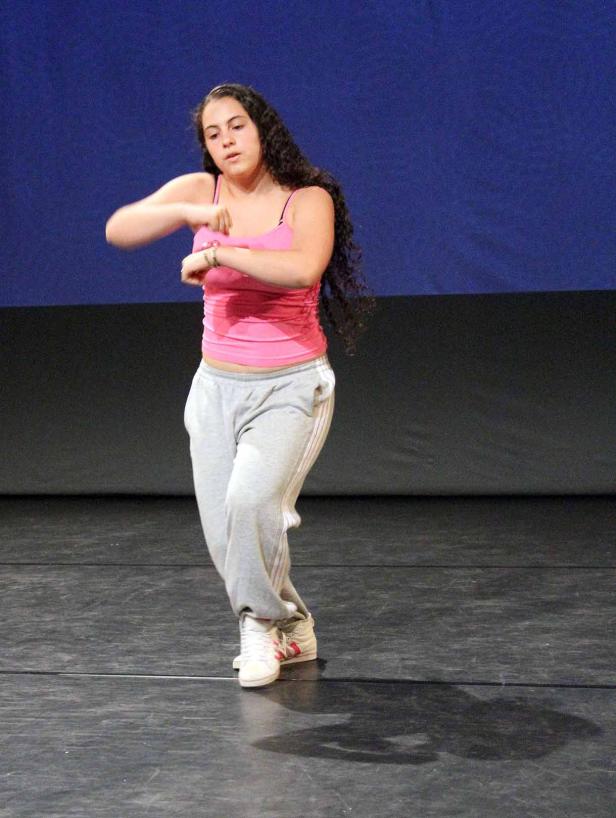 Eine junge Frau tanzt in einem rosa Top und grauer Jogginghose auf einer Bühne.