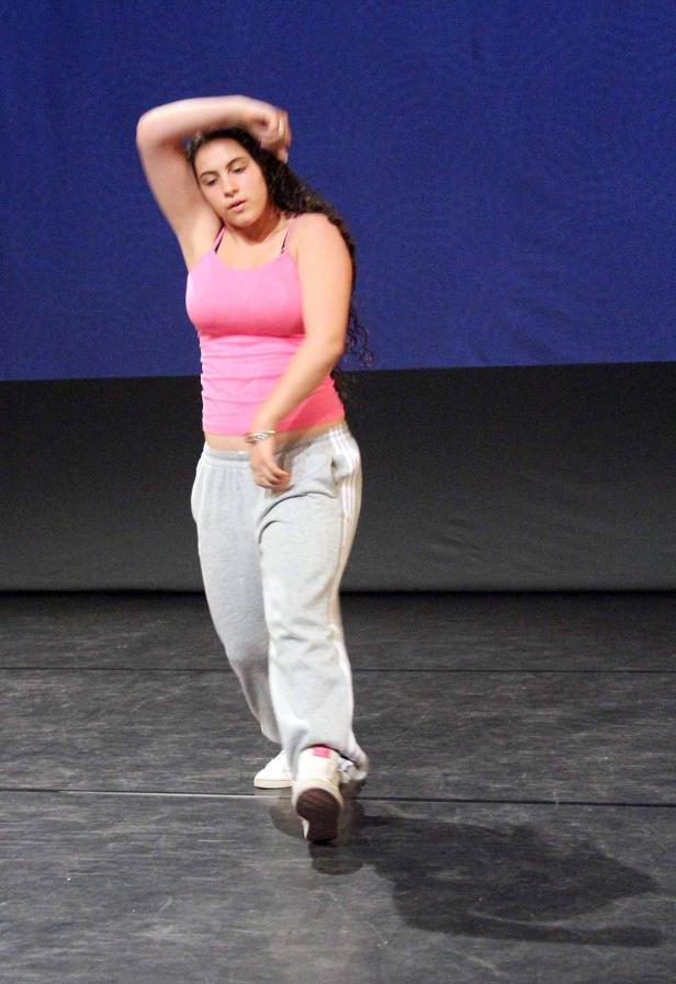 Eine junge Frau tanzt in einem rosa Top und grauer Jogginghose auf einer Bühne.