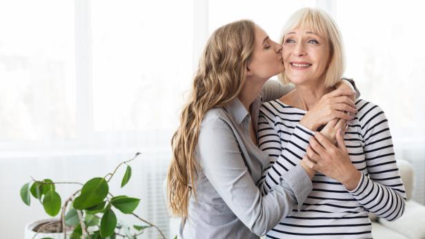 Eine Tochter küsst ihre reife Mutter auf die Wange.