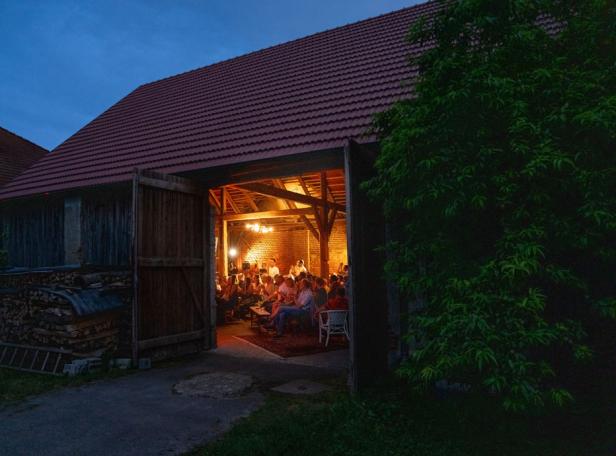 Menschen sitzen abends in einer Scheune und genießen die gemütliche Atmosphäre.
