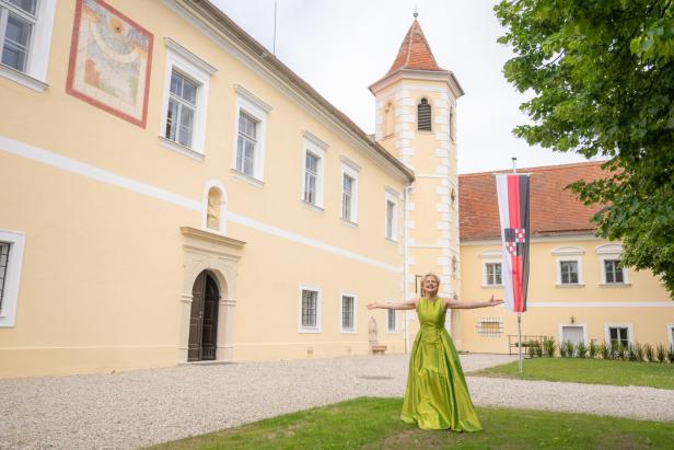 Eine Frau in einem grünen Kleid steht vor einem gelben Schloss mit einem Turm.