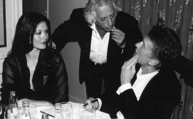 Catherine Zeta-Jones und zwei Männer sitzen an einem Tisch bei einer Veranstaltung.