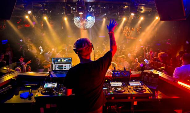 Ein DJ legt in einem Nachtclub vor tanzenden Menschen auf.