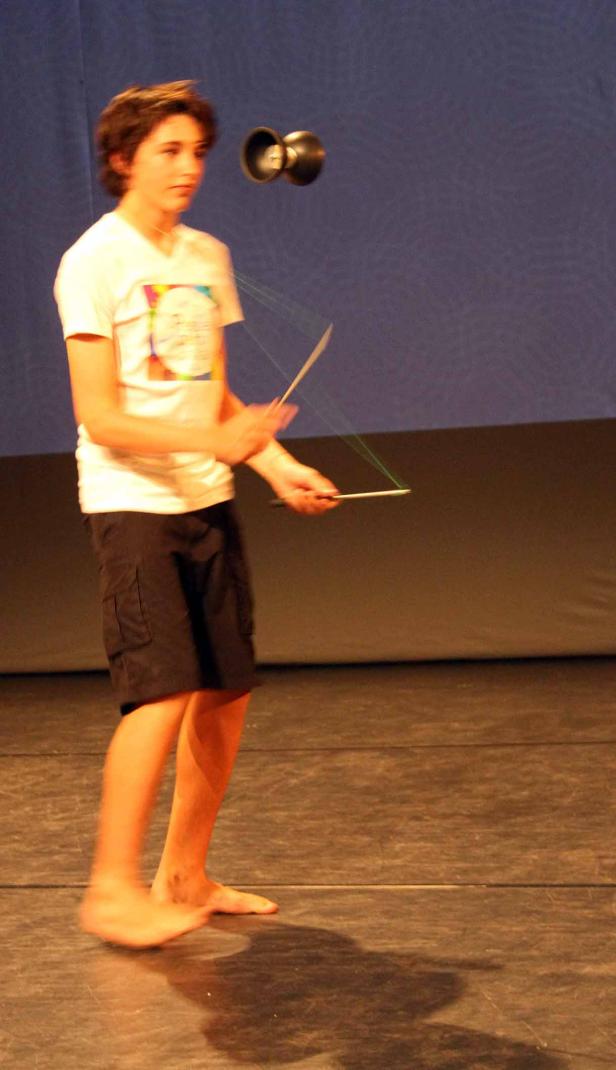 Ein barfüßiger Junge spielt mit einem Diabolo auf einer Bühne.