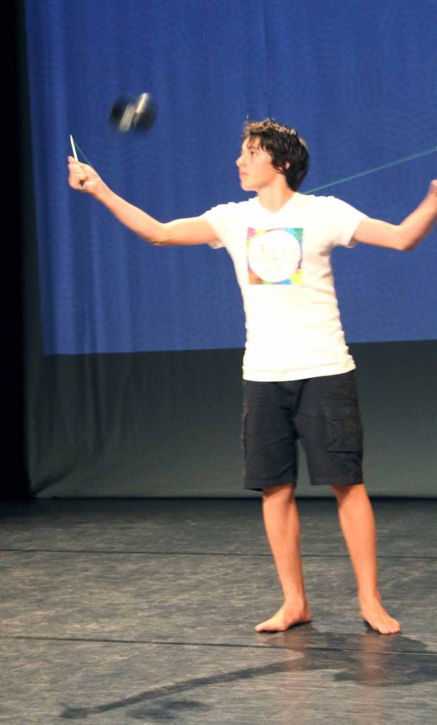 Ein barfüßiger Junge führt auf einer Bühne Tricks mit einem Kendama vor.