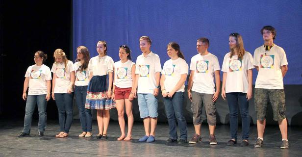 Eine Gruppe junger Leute steht auf einer Bühne und trägt T-Shirts mit der Aufschrift „Peace Camp 2013“.