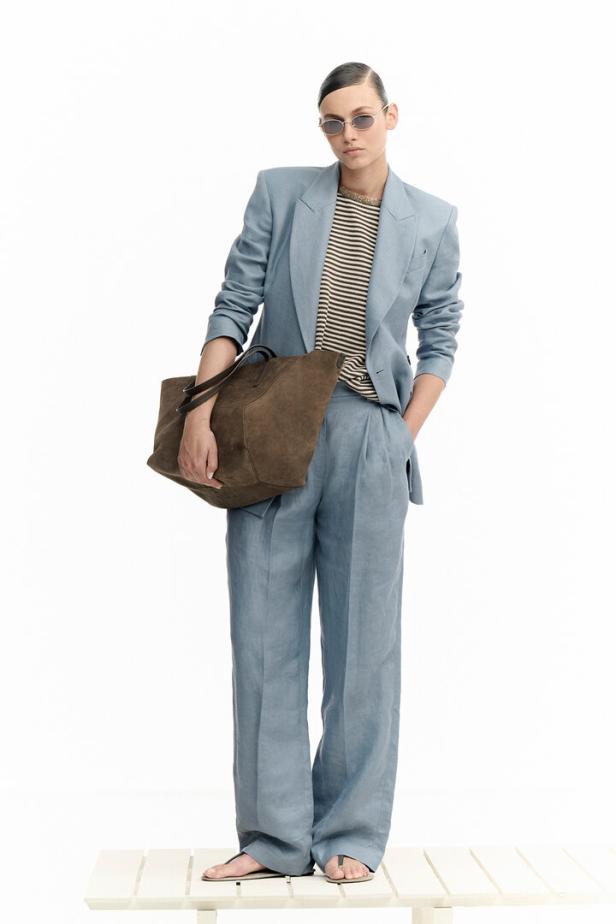 Eine Frau in einem hellblauen Hosenanzug mit einer braunen Handtasche.