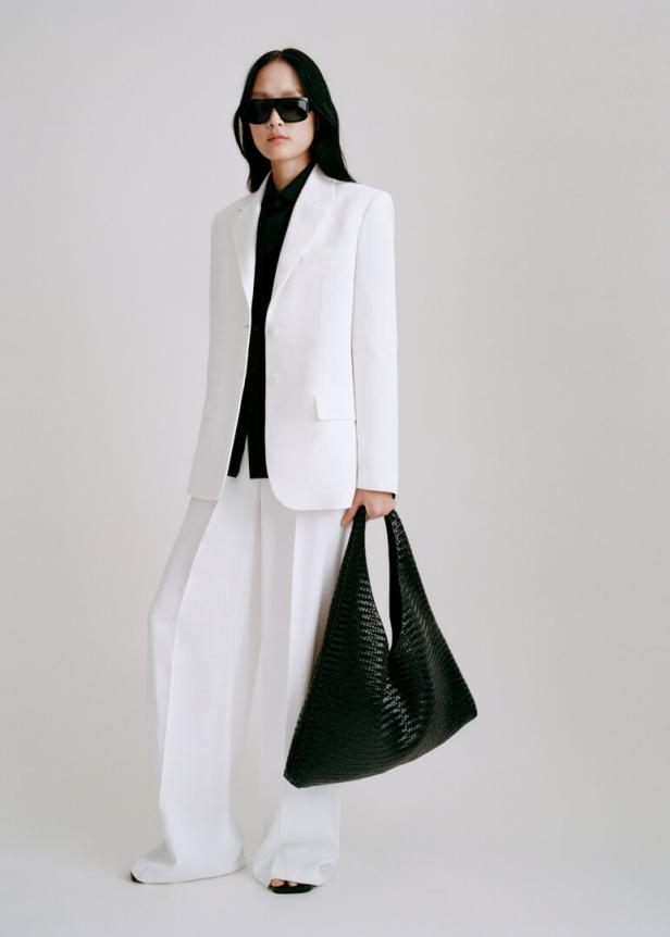 Eine Frau mit Sonnenbrille trägt einen weißen Hosenanzug und eine schwarze Tasche.