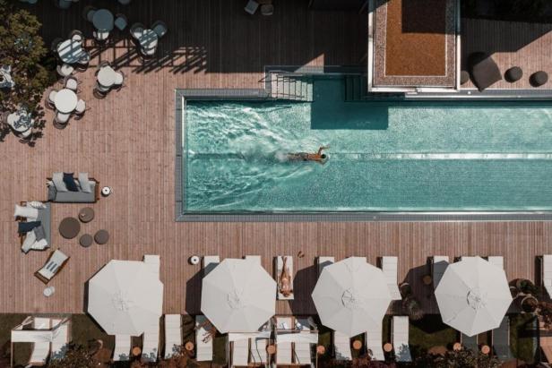 Luftaufnahme eines Schwimmers in einem Pool, umgeben von Liegestühlen und Tischen.