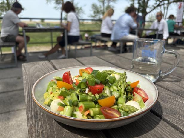 Ein Teller mit Spargelsalat und Cherrytomaten auf einem Holztisch.