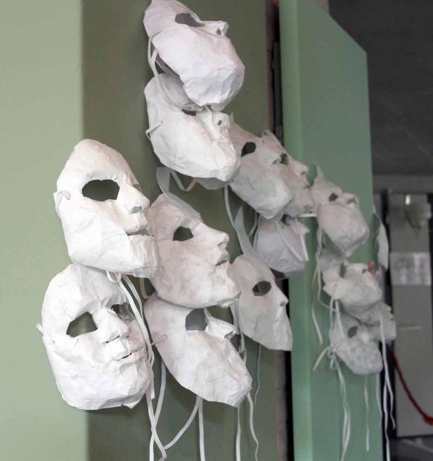 Mehrere weiße, unbemalte Masken hängen an einer grünen Wand.