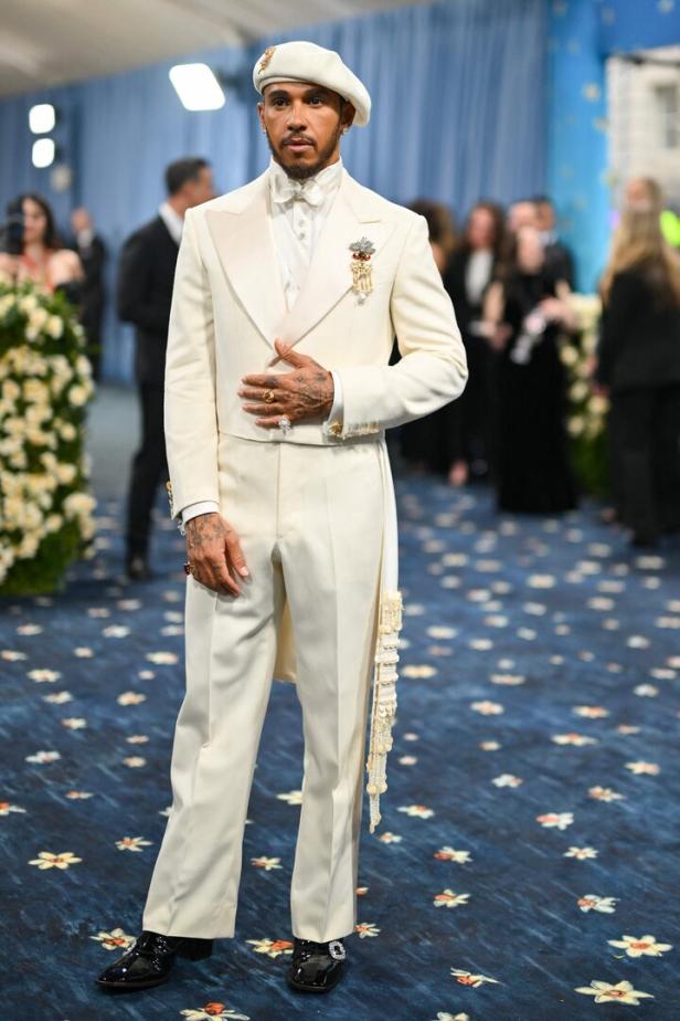 Lewis Hamilton in einem weißen Anzug und einer Baskenmütze auf dem roten Teppich der Met Gala.