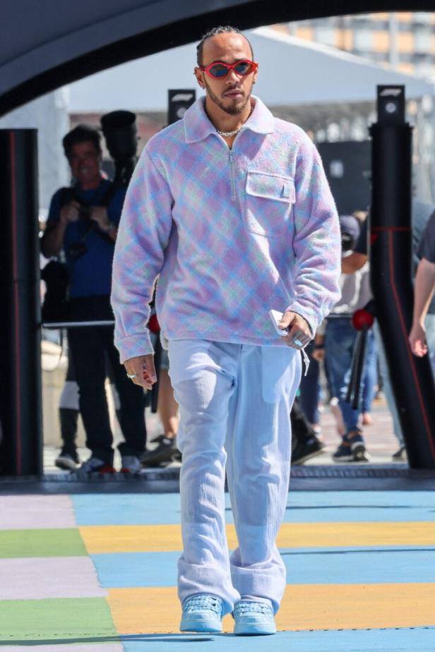 Lewis Hamilton mit roter Sonnenbrille und farbenfrohem Pullover bei einem Formel-1-Rennen.