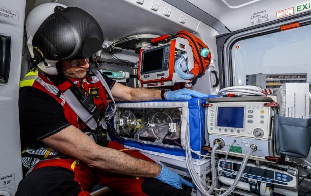 Ein Mann in einer rot-schwarzen Uniform sitzt im hinteren Teil eines Hubschraubers.