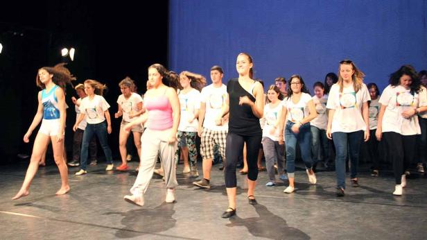 Eine Gruppe junger Leute tanzt barfuß auf einer Bühne.