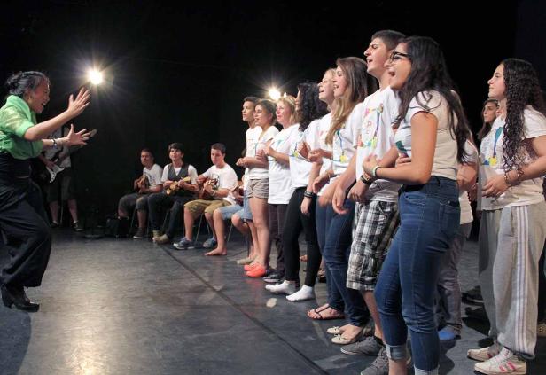 Eine Gruppe von Jugendlichen singt auf einer Bühne unter der Leitung einer Frau.