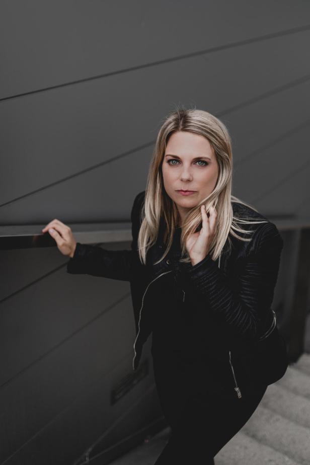 Eine blonde Frau steht in schwarzen Klamotten auf einer Treppe.