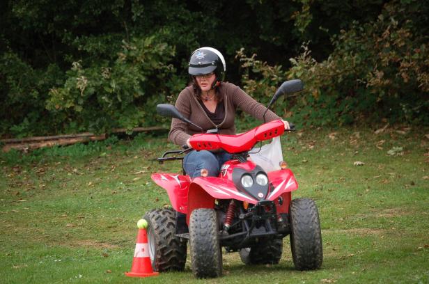 Eine Frau mit Helm fährt ein rotes Quad auf einer Wiese.