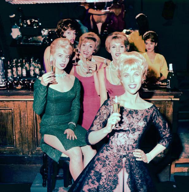 Eine Gruppe junger Frauen sitzt mit Champagnergläsern in der Hand an der Bar.