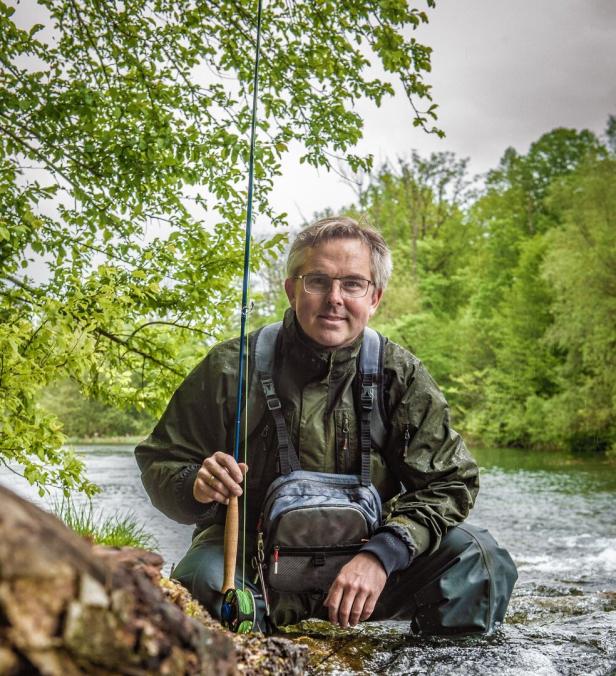 Ein Mann hockt mit einer Angelrute in einem Fluss.