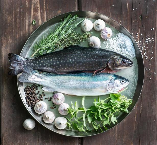 Zwei rohe Fische liegen auf einem silbernen Teller mit Kräutern und Gewürzen.