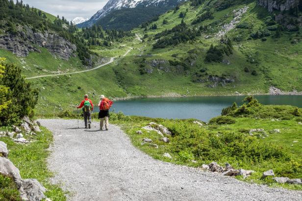 Zwei Wanderer auf einem Weg in den Bergen an einem See.