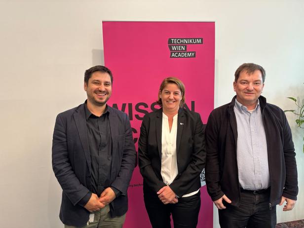 Drei Personen stehen vor einem Technikum Wien Academy Roll Up.
