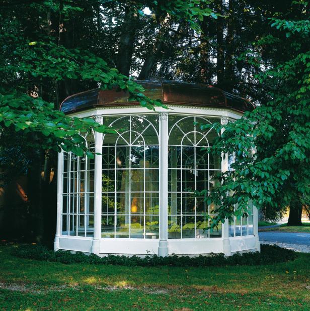 Ein weißes Gartenhaus mit vielen Fenstern steht im Grünen.