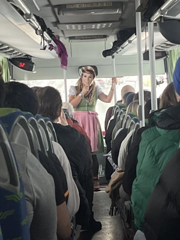 Eine Frau im Dirndl steht in einem Bus voller Fahrgäste.