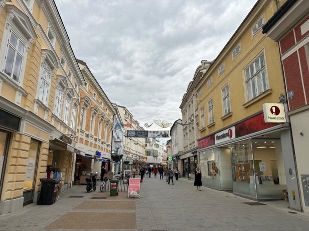 Eine belebte Fußgängerzone mit gelben Gebäuden an einem bewölkten Tag.