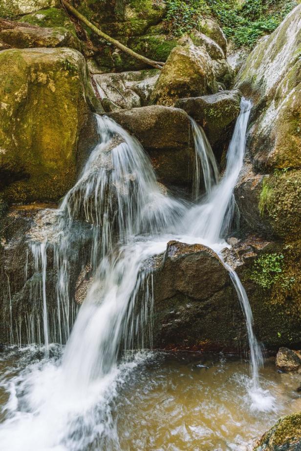 Ein kleiner Wasserfall fließt über moosbewachsene Felsen.