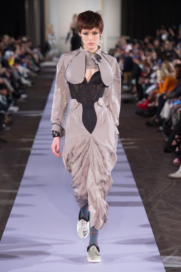 Eine Frau läuft in einem extravaganten, grau-schwarzen Outfit über einen Laufsteg.