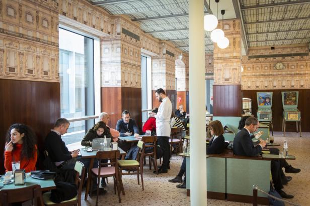 Menschen sitzen in einem Café mit dekorativen Wänden und genießen ihre Getränke.