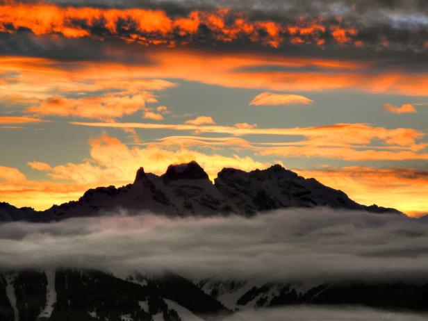 Eine Bergkette ragt bei Sonnenaufgang aus einer Wolkendecke.