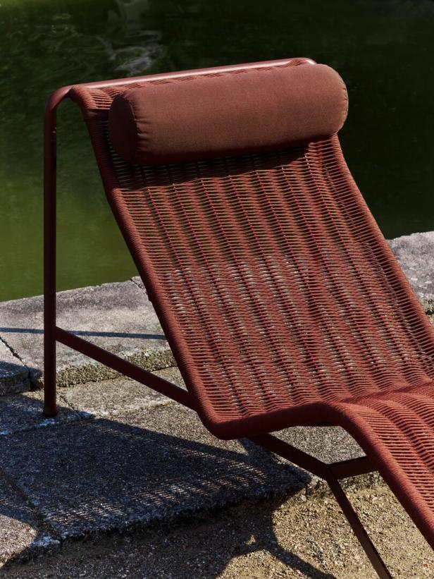 Eine braune Sonnenliege mit Kopfkissen steht im Freien neben einem Teich.