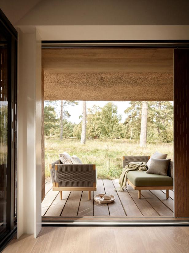 Zwei Sessel mit Kissen stehen auf einer Holzterrasse mit Blick auf eine Wiese und Bäume.