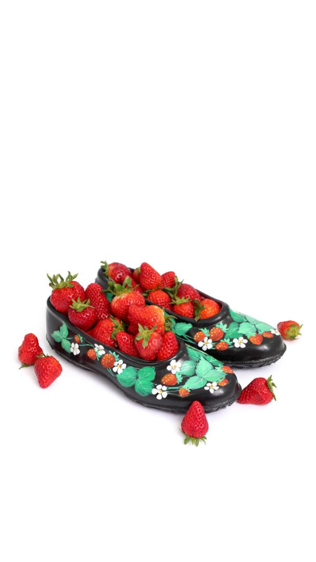 Zwei bemalte Galoschen sind mit frischen Erdbeeren gefüllt.