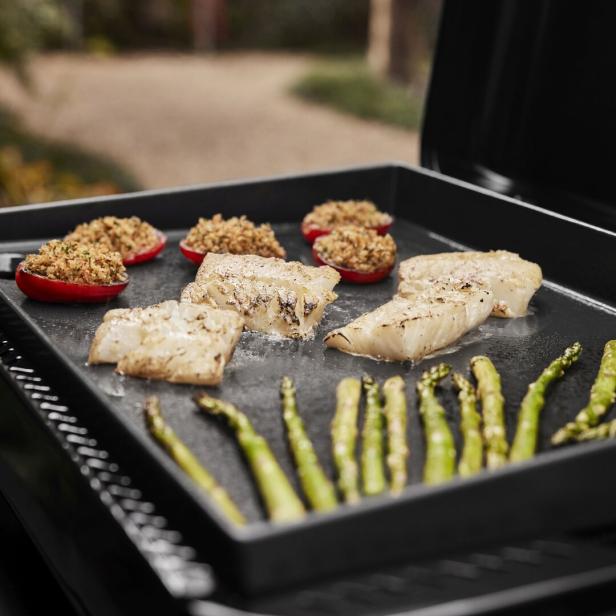 Auf einer Grillplatte liegen Fisch, gefüllte Tomaten und Spargel.