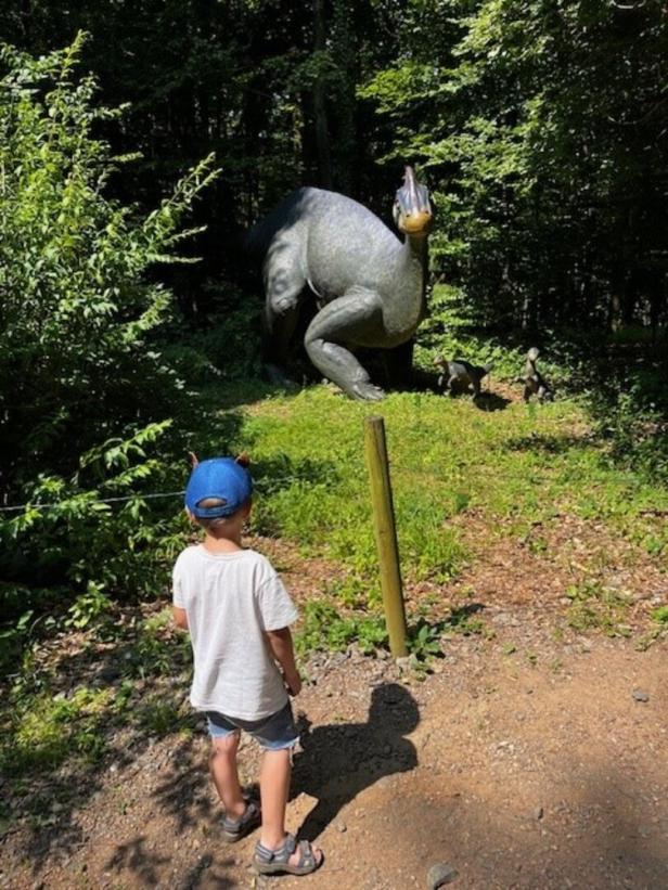 Ein Kind betrachtet eine große Dinosaurierstatue im Wald.