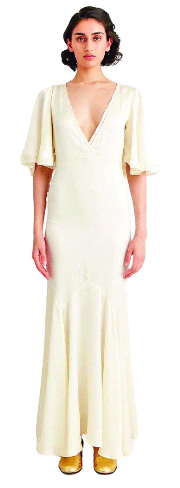 Eine Frau trägt ein elfenbeinfarbenes Kleid mit Trompetenärmeln und goldene Schuhe.