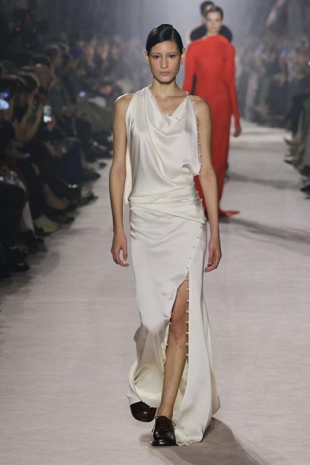 Ein Model präsentiert ein elfenbeinfarbenes Seidenkleid mit Schlitz auf dem Laufsteg.