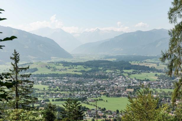 Blick auf eine Stadt in einem Tal, umgeben von grünen Hügeln und Bergen.