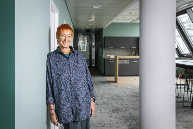 Eva Rossmann steht in einem Bürogebäude an einer Wand.