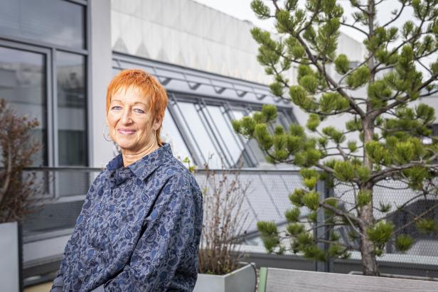 Eva Rossmann sitzt im Freien vor einem Gebäude.