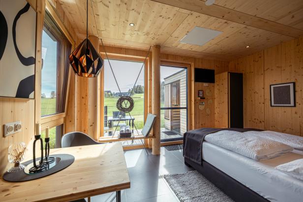 Ein modernes Holzzimmer mit Bett, Tisch und Blick auf eine grüne Landschaft.