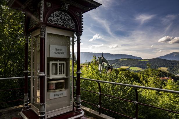 Ein Thermohygrograph und Barograph in einem Schaukasten mit Blick auf eine grüne Landschaft.